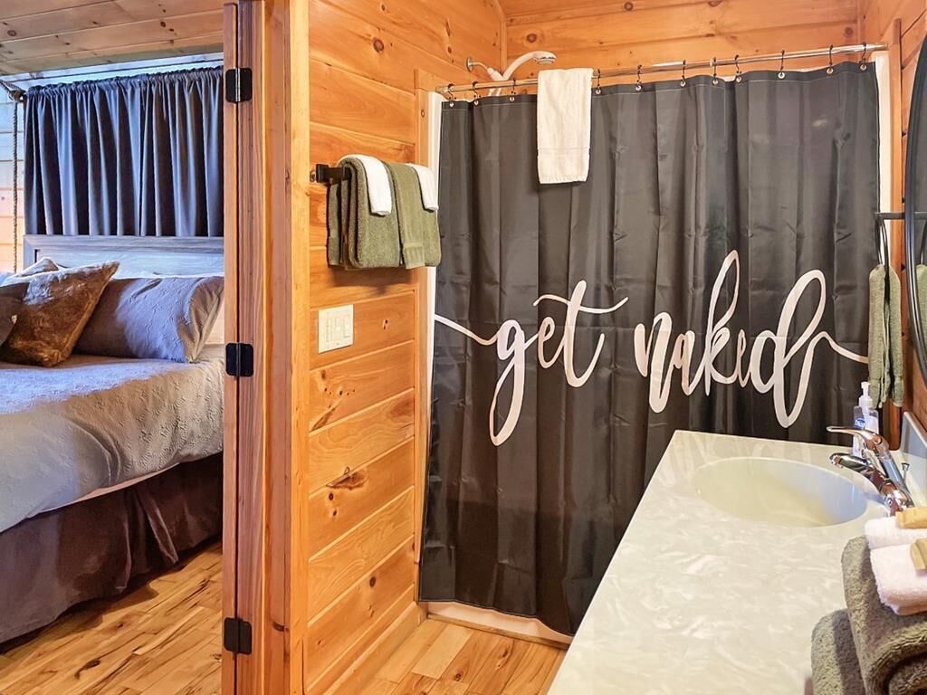 Interieur van een houten chalet met een bed, een douchegordijn met de tekst 'get naked' en een badkamer met een wastafel.