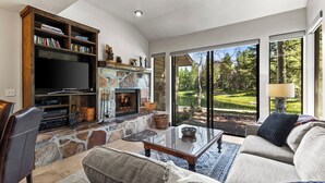 Ein Wohnzimmer mit Kamin aus Stein, einem Fernseher und einem großen Fenster mit Blick auf einen Golfplatz.