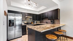 Eine moderne Küche mit Edelstahlkühlschrank, eingebauter Mikrowelle, Gasherd und einer großen Kochinsel mit Barhocker.