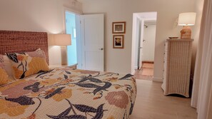 A bedroom with a floral bedspread, a wicker nightstand with a lamp, and a door leading to another room. - WHATA VIEW! Sanibel Siesta Unit #212 (Sanibel)