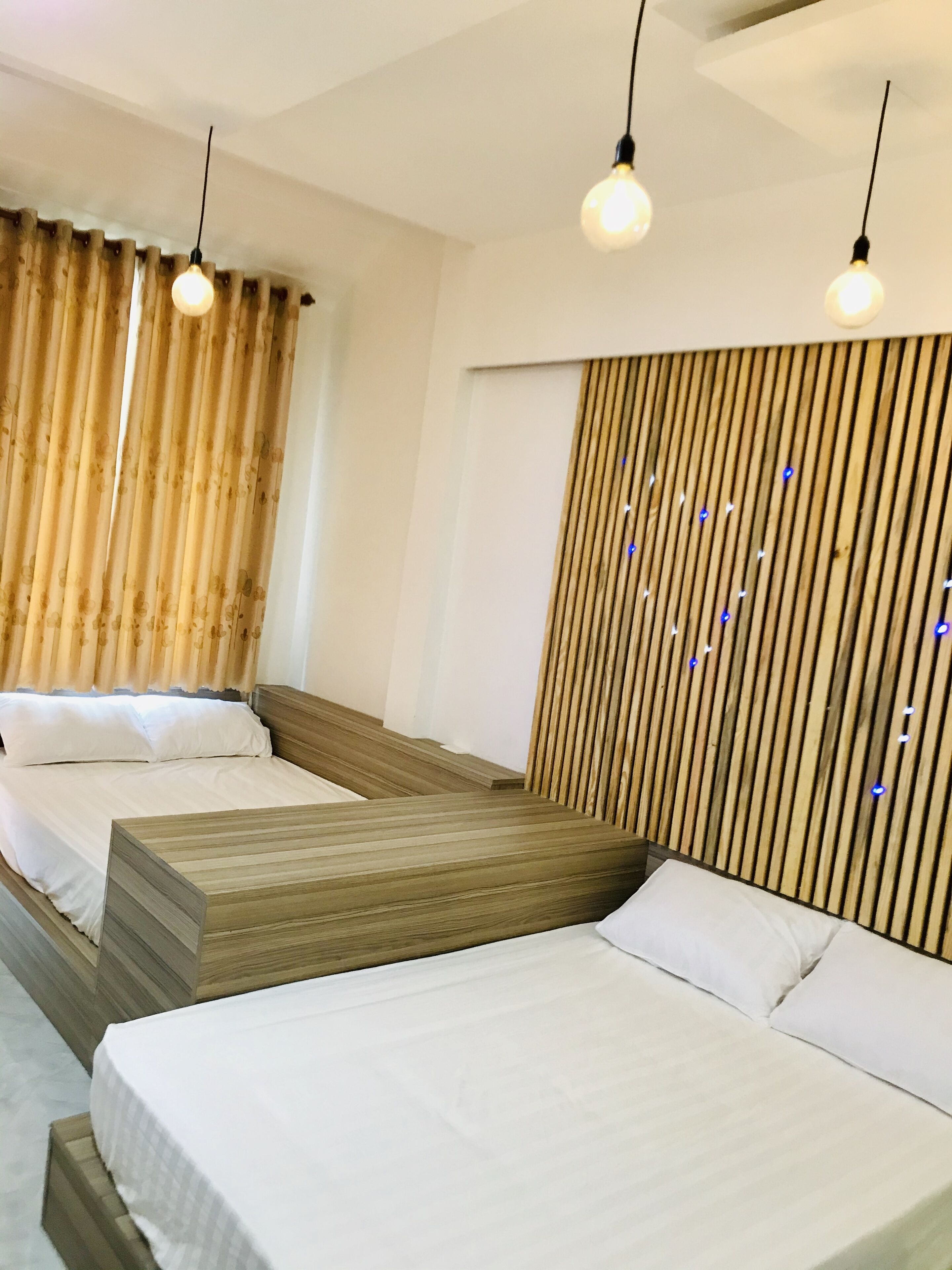 A hotel room with three beds, wooden headboards, and a slatted wooden wall.