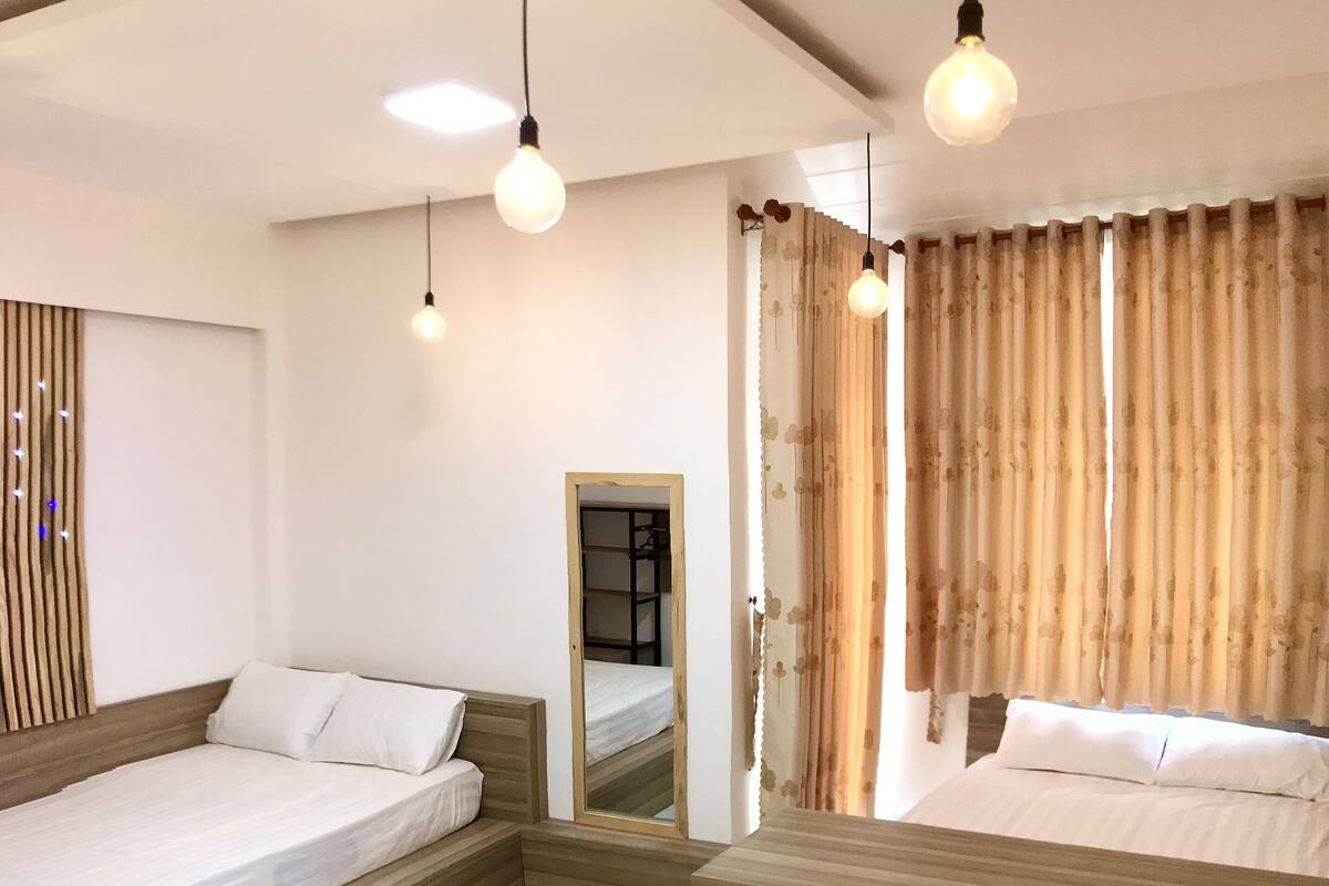 A hotel room with two beds, a wooden headboard, a mirror, and a window with curtains.