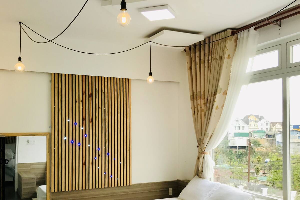 A hotel room with two beds, a wooden slat wall, a large window with a view, and a mirror.