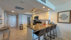 A modern kitchen with a central island, bar stools, a microwave, and a refrigerator.
