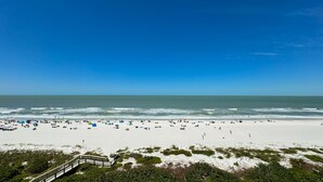 A beach with a wooden boardwalk leading to a sandy area with umbrellas and beachgoers.