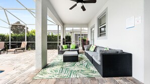 A covered patio area with a ceiling fan, outdoor furniture, and a view of a house in the background.