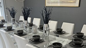 A modern dining room with a glass table, white chairs, and black bowls.