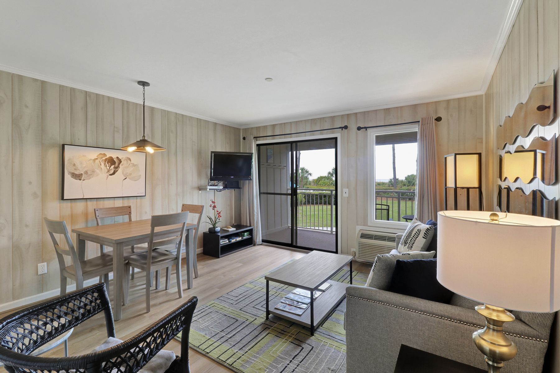 A modern living room with a dining area, a TV, and a balcony with a view.