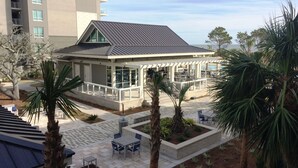 A modern building with a covered patio area, outdoor seating, and palm trees. - Oceanfront Paradise! Heated Beachside Pool (Hilton Head)