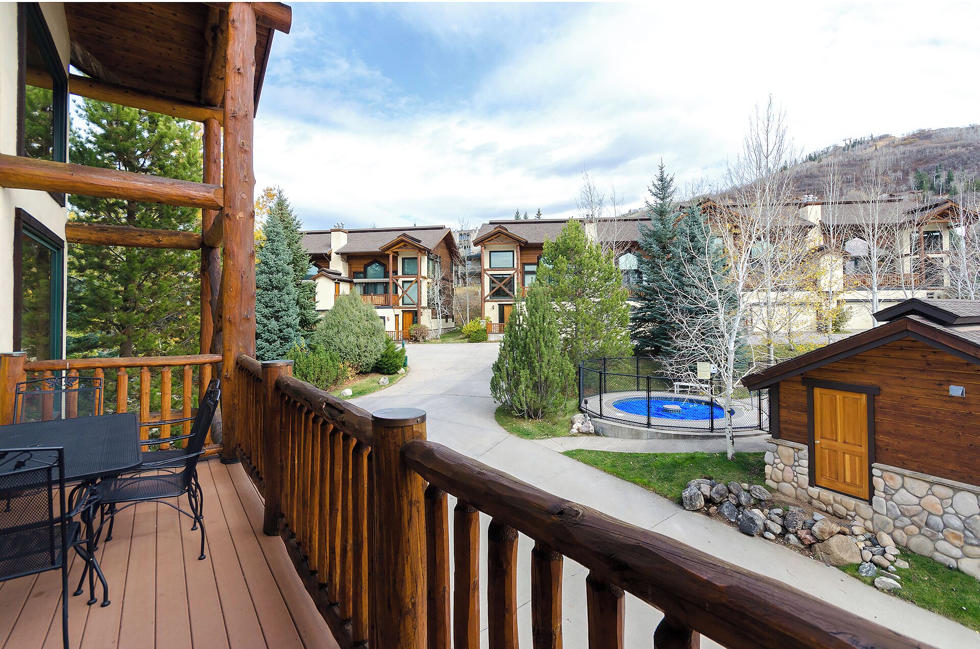 Une terrasse en bois avec des meubles d’extérieur, un mur en pierre et une vue sur un quartier résidentiel avec des maisons et des arbres.