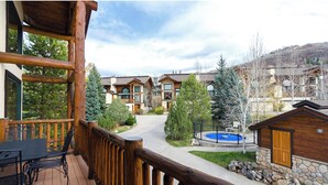 A wooden deck with outdoor furniture, a stone wall, and a view of a residential area with houses and trees.