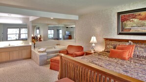 Une chambre spacieuse avec un grand lit, un coin salon et une salle de bain équipée d’une baignoire et d’un grand miroir.
