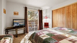 Une chambre avec un grand lit, un téléviseur posé sur un meuble, une armoire en bois et une porte-fenêtre coulissante donnant sur un balcon.