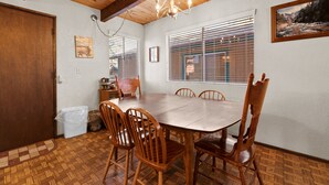 Une salle à manger avec une table et des chaises en bois, un lustre et une fenêtre avec des stores.
