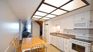 Une cuisine avec une table à manger en bois, des placards blancs, un four à micro-ondes et un four traditionnel.
