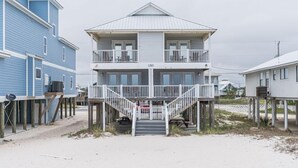 A two-story beach house with a balcony and a staircase leading to the entrance. - Beach Front Duplex with Gulf Views | Sleeps 11 (Gulf Shores)