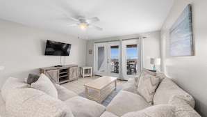 A living room with a sofa, a coffee table, a TV, and a ceiling fan. - Beach Front Duplex with Gulf Views | Sleeps 11 (Gulf Shores)