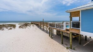 A beach house with a wooden deck extending to the ocean, a covered outdoor seating area, and a large window overlooking the sea. - Beach Front Duplex with Gulf Views | Sleeps 11 (Gulf Shores)