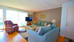 Una sala de estar con sofá, sillón, mesa de centro, televisor y una puerta.
