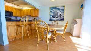 Un comedor con una mesa y sillas de madera, una cocina con armarios de madera, y un cuadro de un velero en la pared.