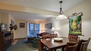 A dining area with a wooden table and chairs, a painting on the wall, and a view through a glass door. - SHB26 | Minutes from Slopes | Free City Bus | Hot Tub (Steamboat Springs)
