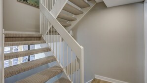 A staircase with beige carpeted steps and white railings, leading to a landing with a ceiling light. - Stunning Pool Views! Close to Coligny Plaza/Beach (Hilton Head Island)