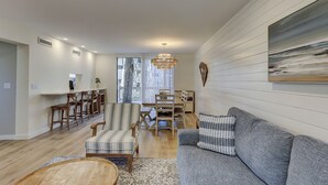 A spacious living room with a large gray sofa, striped armchairs, a wooden coffee table, and a chandelier. - Stunning Pool Views! Close to Coligny Plaza/Beach (Hilton Head Island)