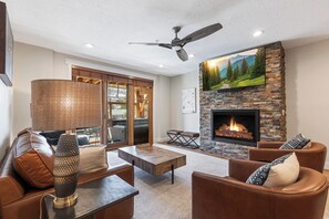 A modern living room with leather furniture, a fireplace, and a large window overlooking a deck.