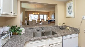 A kitchen with granite countertops, a double sink, and a dishwasher. There is a potted plant and a coffee maker on the counter. - Heated Oceanfront Pool with Hot Tub! Close to Coligny! (Hilton Head)