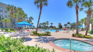 A pool area with lounge chairs, umbrellas, and palm trees. - Heated Oceanfront Pool with Hot Tub! Close to Coligny! (Hilton Head)