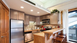 Una cocina moderna con armarios de madera, electrodomésticos de acero inoxidable, encimera de granito y una zona de bar con taburetes.