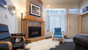 Una sala de estar con chimenea, un sillón azul, un sofá de cuero negro y una alfombra blanca y mullida.