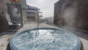 Un jacuzzi en una terraza de madera con vista a un edificio y un cielo nublado.