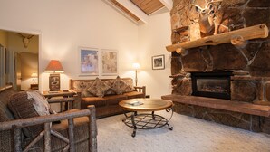 A cozy living room with a stone fireplace, a wooden ceiling, and a comfortable seating area with a coffee table.
