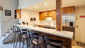 A modern kitchen with a central island, bar stools, wooden cabinets, stainless steel appliances, and a built-in microwave.
