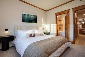 A bedroom with a large bed, a nightstand, a wall-mounted light, and a painting of a forest.