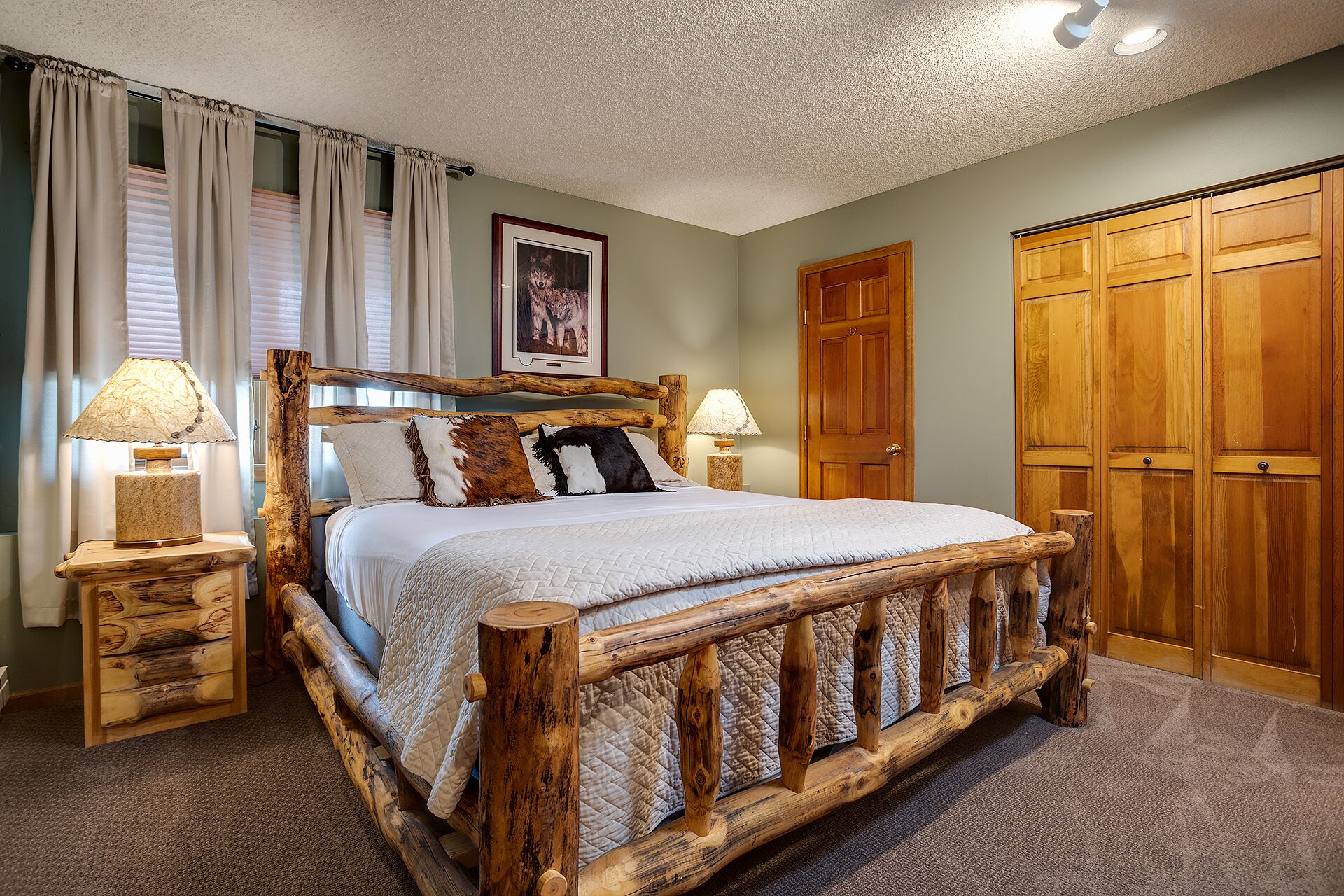 A wooden bed with a headboard, two bedside tables with lamps, a large wooden wardrobe, and a framed picture on the wall.