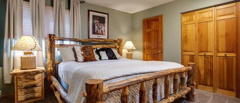 A wooden bed with a headboard, two bedside tables with lamps, a large wooden wardrobe, and a framed picture on the wall.