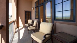 Een balkon met twee stoelen en een tafel, grote ramen met zonwering en uitzicht op het landschap.