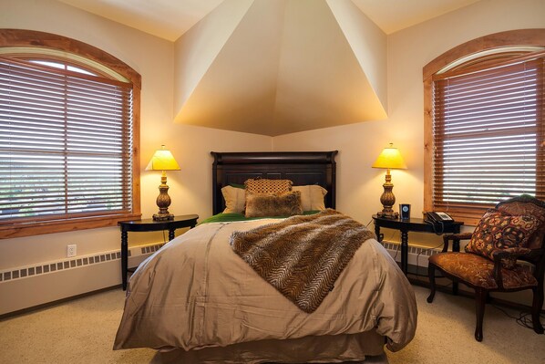 A bedroom with a large bed, two bedside lamps, a chair, and a window with blinds. - HM6A | Opulent Penthouse in Mtn Village | Pool and Hot Tub | A/C (Steamboat Springs)
