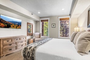 A bedroom with a large bed, a dresser, a chair, and a window with a view of trees. - Great location to Old Town/Main Street| Hot Tub | Managed by Park City Lodging (Park City)