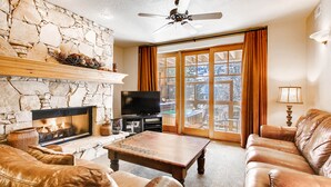 A living room with a stone fireplace, leather furniture, a television, and a large window with curtains. - Managed by Park City Lodging-Great location, just a short walk to Main Street. (Park City)