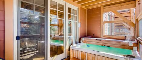 A hot tub area with a wooden deck, a sliding glass door, and a staircase leading to an upper level.