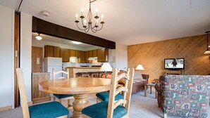 Un comedor con una mesa y sillas de madera, una cocina al fondo y un televisor sobre un mueble.