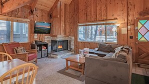 A cozy log cabin interior with a fireplace, wooden walls, a television, and comfortable seating. - Moonridge Hideaway - Fireplace, Deck, Fenced Yard, Pet Friendly (Big Bear Lake)