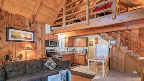 A cozy wooden interior with a sofa, coffee table, kitchen, and staircase. - Moonridge Hideaway - Fireplace, Deck, Fenced Yard, Pet Friendly (Big Bear Lake)