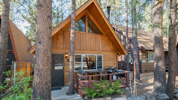 A log cabin with a deck, surrounded by tall trees. - Moonridge Hideaway - Fireplace, Deck, Fenced Yard, Pet Friendly (Big Bear Lake)