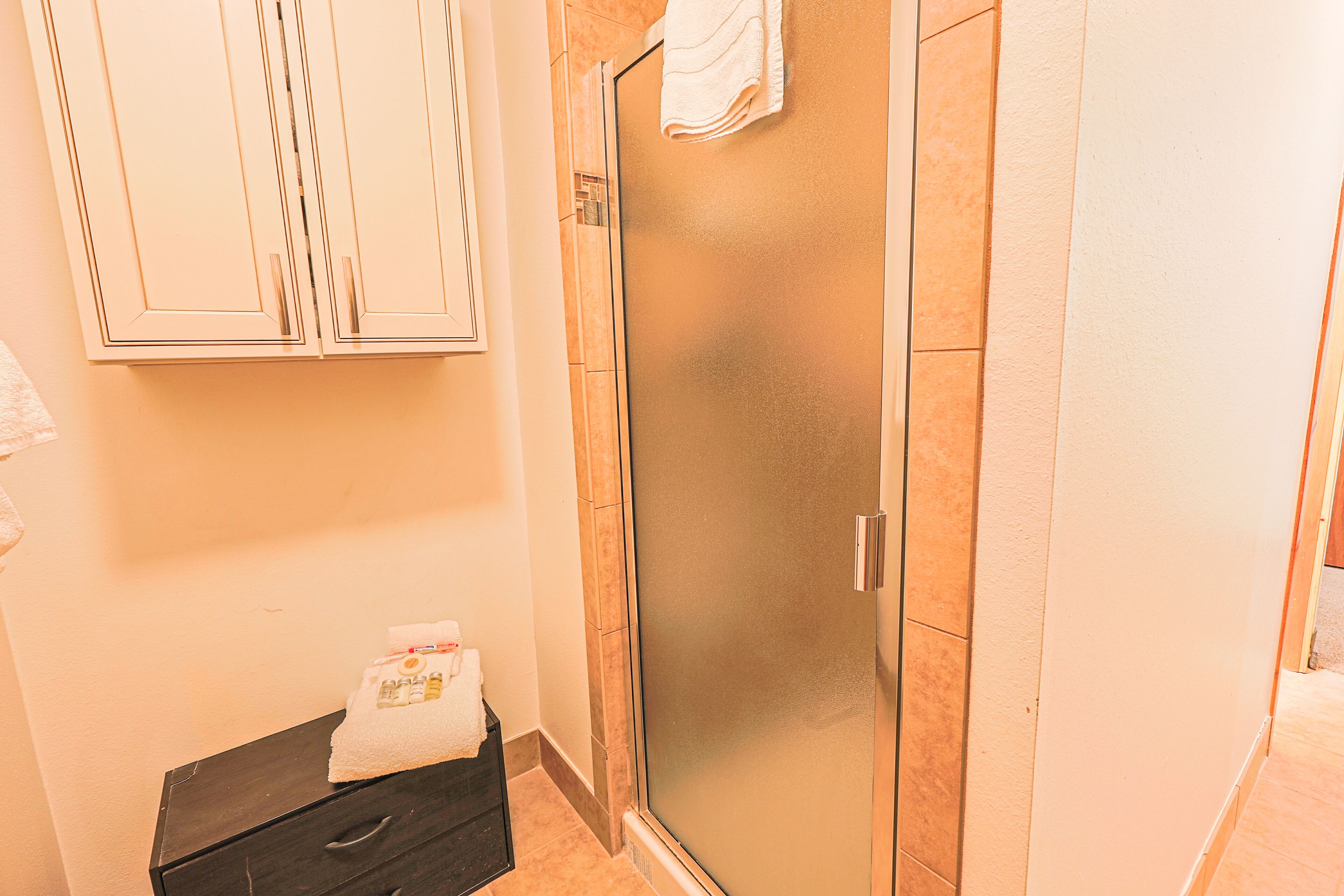 A bathroom with a glass shower door, a towel on the floor, and a cabinet above the shower.