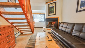 A living room with a wooden staircase, a fireplace, a leather sofa, and a wooden coffee table. - Center Village Ski In/Out Perfectly decorated and sleeps 6 Walk to everything (Copper)