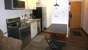 A compact kitchen with a built-in oven, microwave, and refrigerator. There is a dining table with chairs and a hanging light fixture. - Center Village Ski In/Out Perfectly decorated and sleeps 6 Walk to everything (Copper)